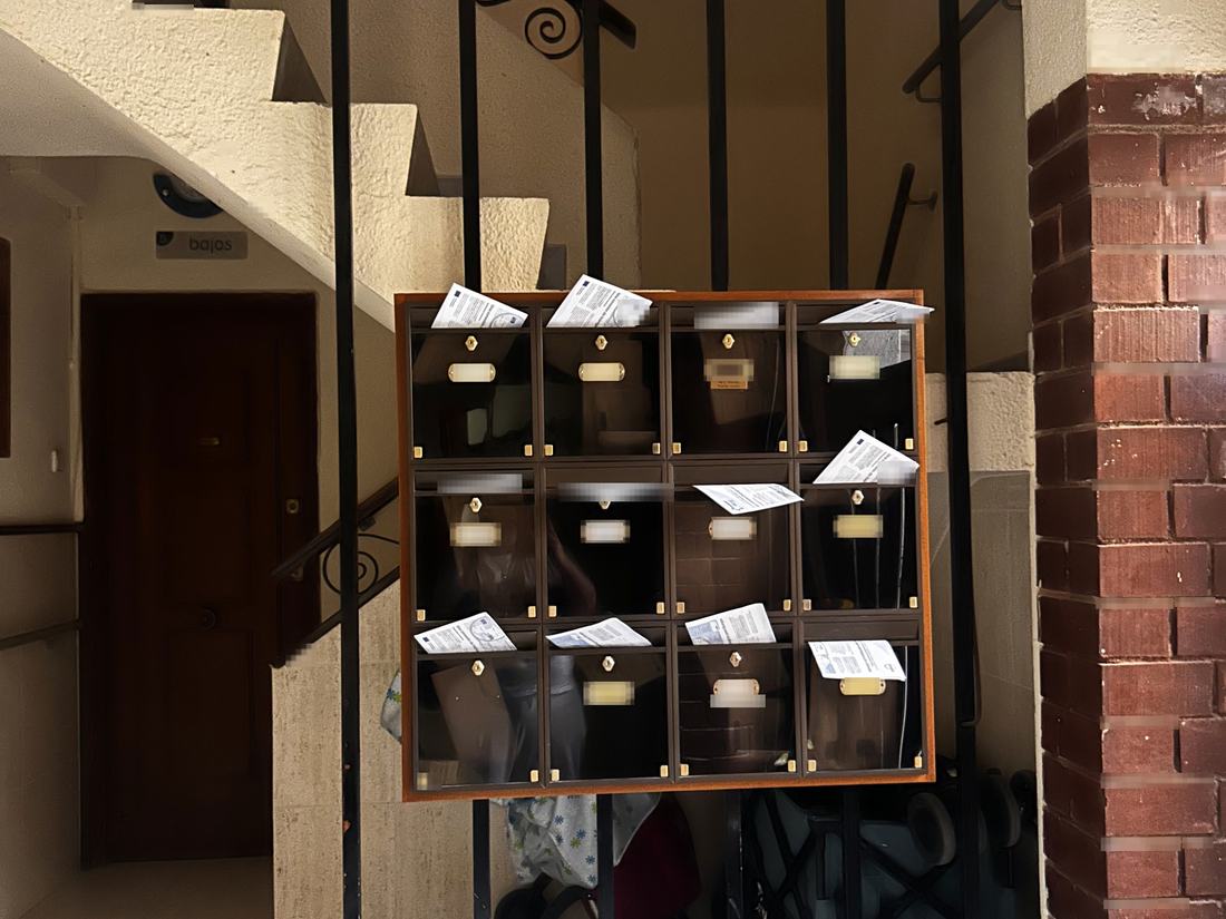 Buzones de madera bajo la escalera de un edificio, con los flyers asomando